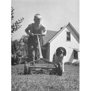 Young Boy Mowing the Lawn with a Simple Mower While His Dog Follows 